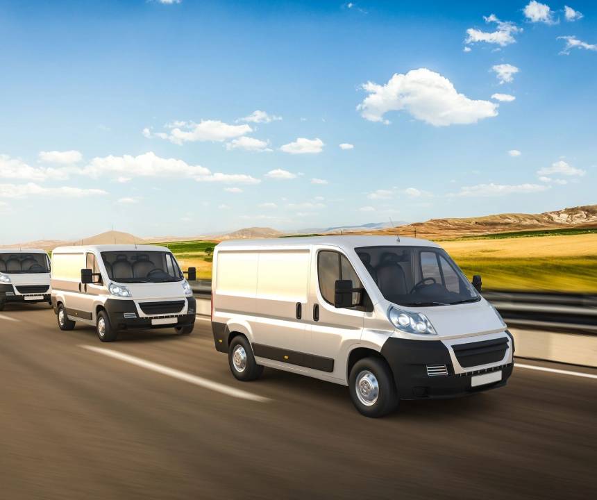 Two vans are driving down the road in a field.